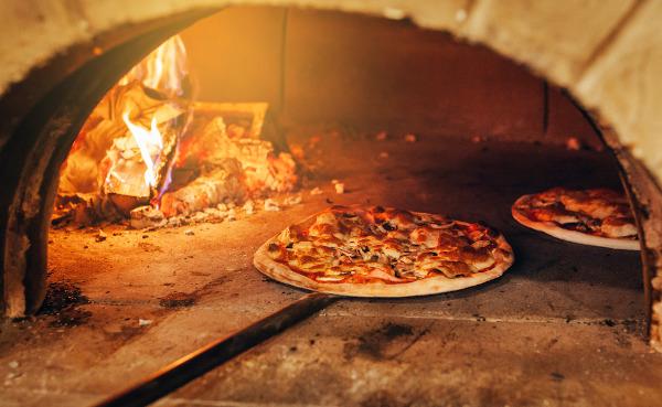 Italian pizza being made in a wood-fired oven, one of the main types of pizza in the history of pizza.