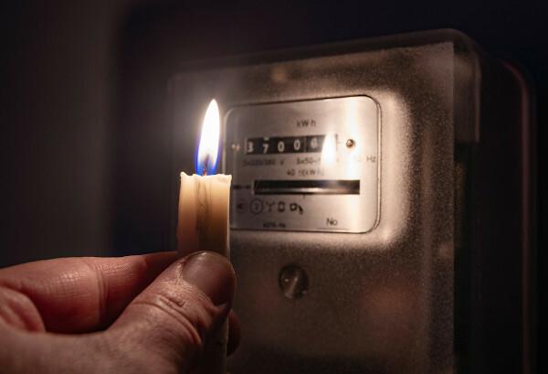 Χέρι που κρατά ένα αναμμένο κερί που φωτίζει το μετρητή κατανάλωσης ηλεκτρικής ενέργειας.