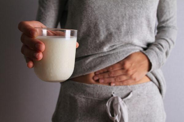 Kvinne med en hånd på magen og med den andre holder et glass melk, mat som kan forårsake gass (flatulens).