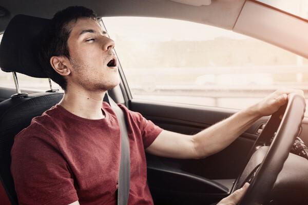 Man slaapt met zijn mond open terwijl hij het stuur vasthoudt, in een auto; narcolepsie kan verkeersongevallen veroorzaken.