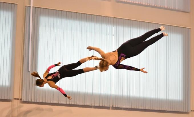 To trampolinegymnaster på trening, hengende i luften, drar ned etter å ha hoppet på en trampoline.