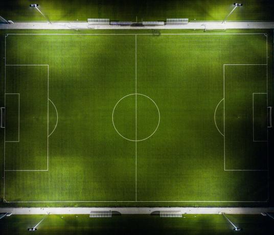 Изглед отгоре на зелен футболен терен с типични бели маркировки.
