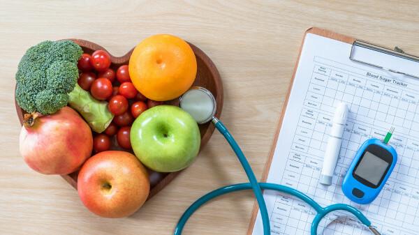 Fruits and vegetables on a heart plate next to a glucometer on a clipboard.