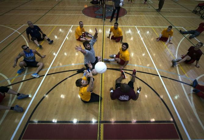 Bovenaanzicht van een zittend volleybalveld, zes spelers aan elke kant en degenen aan de linkerkant die de bal proberen te blokkeren.