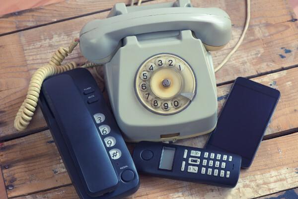 Telephones from different eras, arranged on a wooden surface, representing the evolution of the device