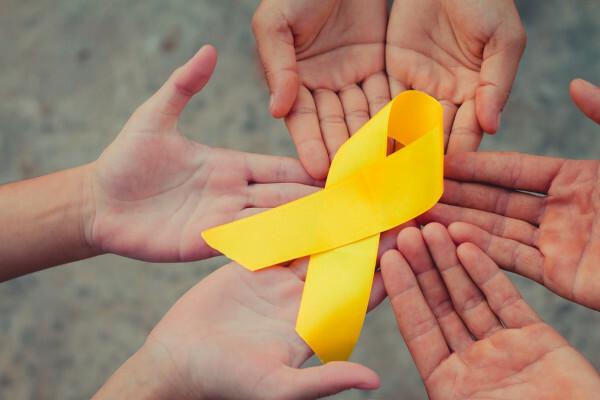 Roke sklenjene in rumena pentlja, simbol svetovnega dneva preprečevanja samomorov in rumenega septembra, nad njimi. 
