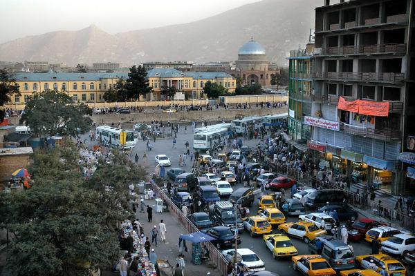 Взгляд на центр города Кабула показывая толпу и автомобили; на заднем плане - мечеть и холмы. 