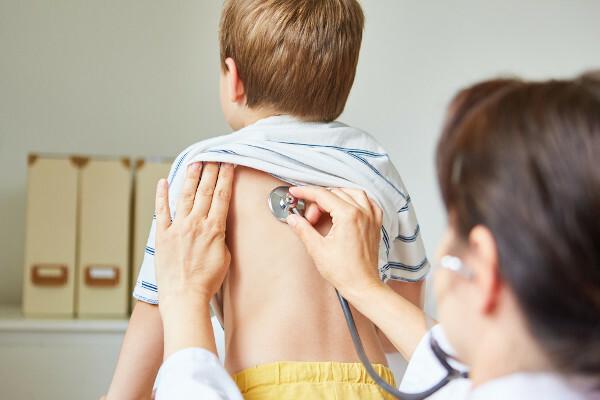 Arts die de rug van een jongen onderzoekt met een stethoscoop; deze test kan bronchospasme identificeren.