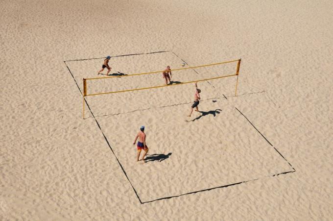 Pohľad zhora na ihrisko plážového volejbalu, kde hrajú dvaja muži a dve ženy.